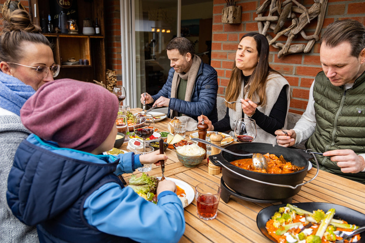 Mehrere Männer und Frauen und ein Kind sitzen draußen an einem gedeckten Tisch und essen