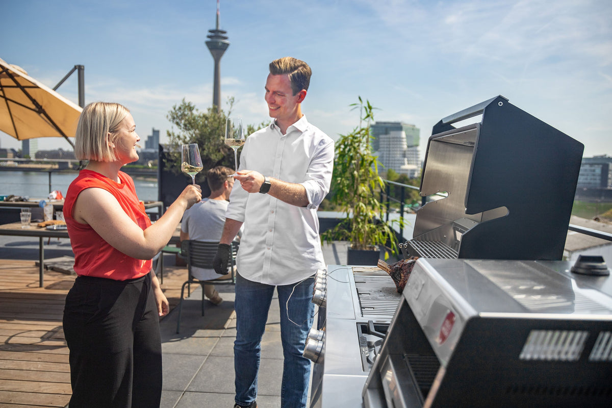 Eine blonde Frau und ein blonder Mann stoßen auf einer Dachterrasse vor einem offenen Otto Wilde G32 Connected an